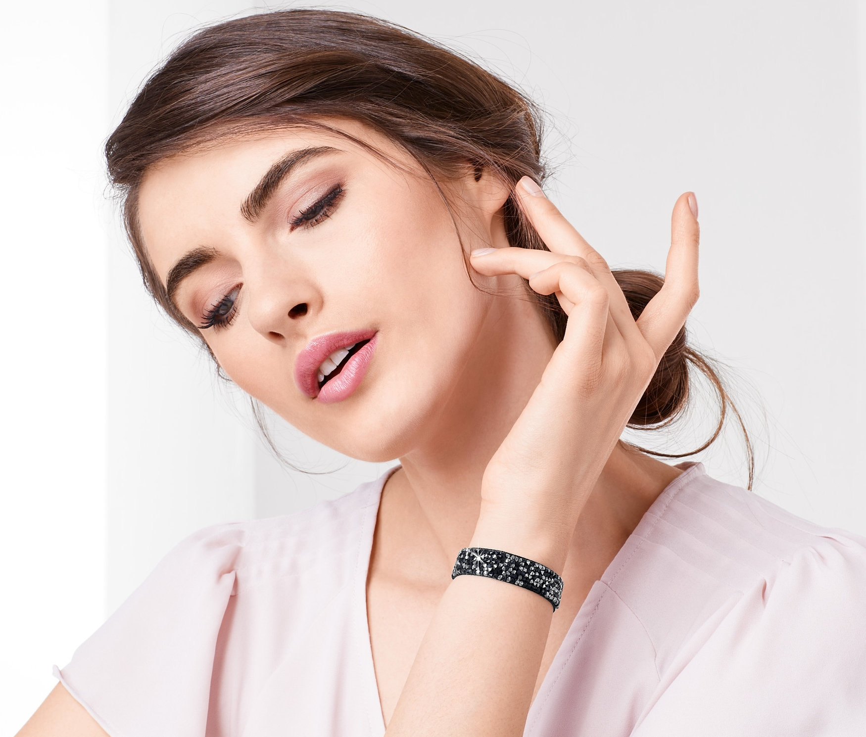 Kadın yüzüne dokunuyor ve ışıltılı bir bileklik takıyor.