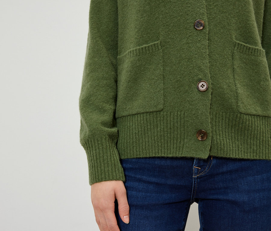 Kahverengi düğmeli ve cepli zeytin yeşili bir hırka ve koyu mavi kot pantolon giyen bir kadının yakın çekimi.