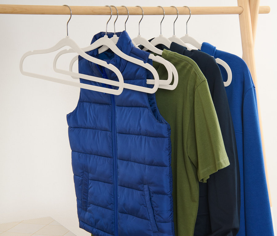 Mavi yelek ve tişörtler, ahşap bir askılık üzerinde askılarda duruyor.