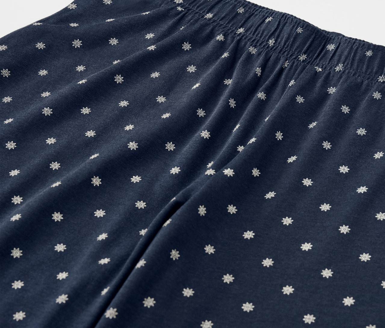 Beyaz çiçekli ve lastikli belli, lacivert bir pantolonun yakın çekimi.