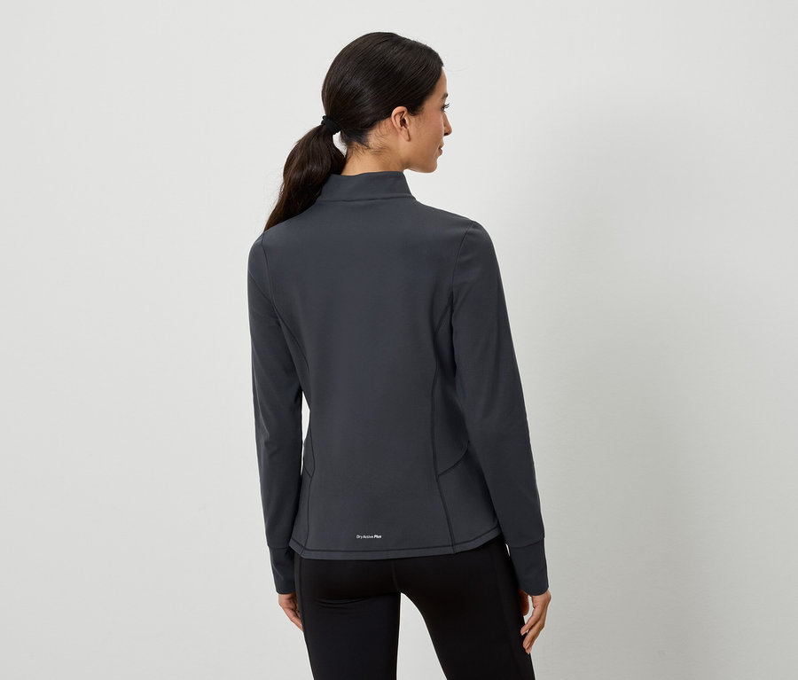 Kahverengi saçları at kuyruğu yapılmış bir kadın, kameraya arkası dönük şekilde poz veriyor. Gri bir spor ceket ve siyah tayt giyiyor.