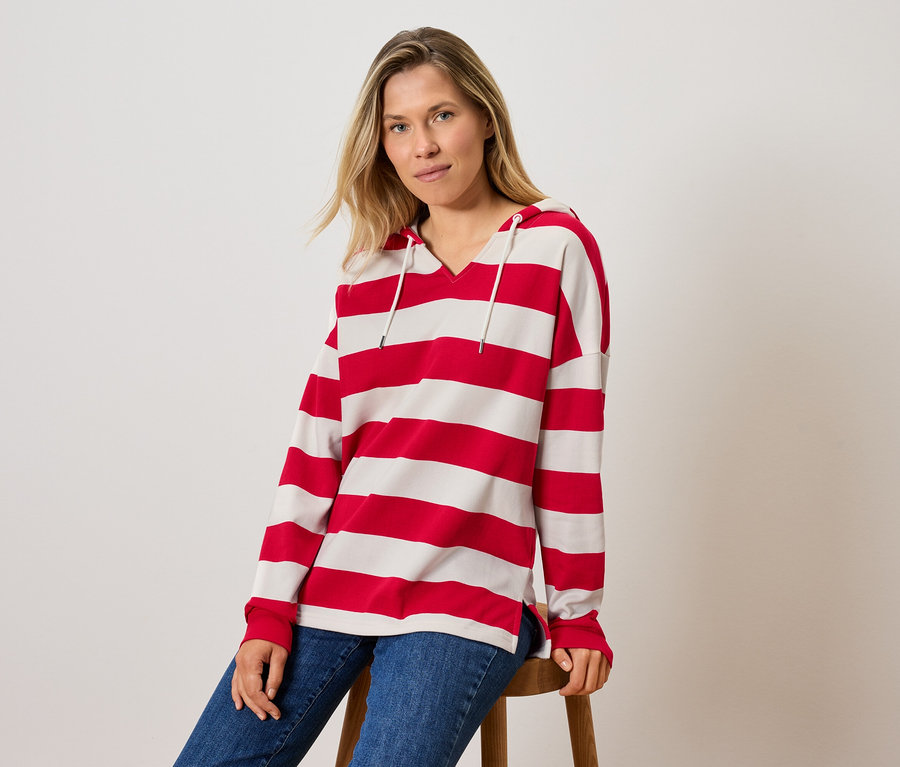 Bir kadın taburede oturuyor, çizgili kapüşonlu bir sweatshirt ve kot pantolon giyiyor.