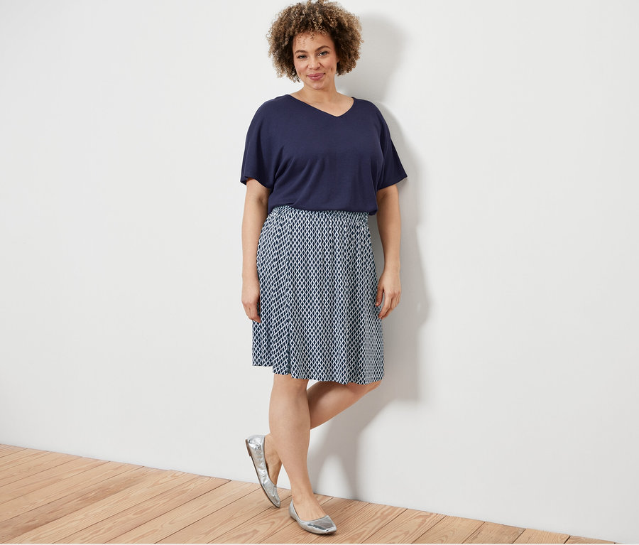 Kadın lacivert dokulu tişört ve baskılı jarse etekle poz veriyor.