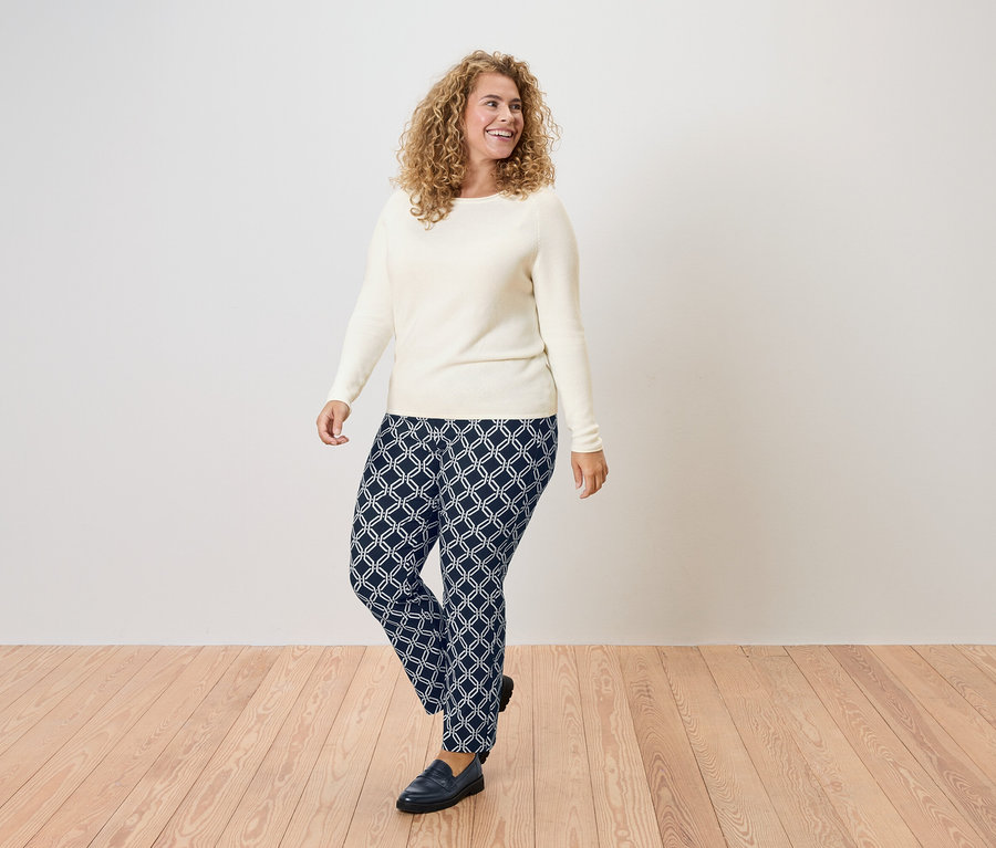Kıvırcık saçlı, krem rengi bir kazak ve geometrik desenli lacivert pantolon giyen bir kadın.