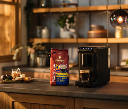 Mutfak tezgahında bir kahve makinesi, bir fincan kahve ve bir paket BARISTA Origins Colombia - 1 kg çekirdek kahve bulunmaktadır.