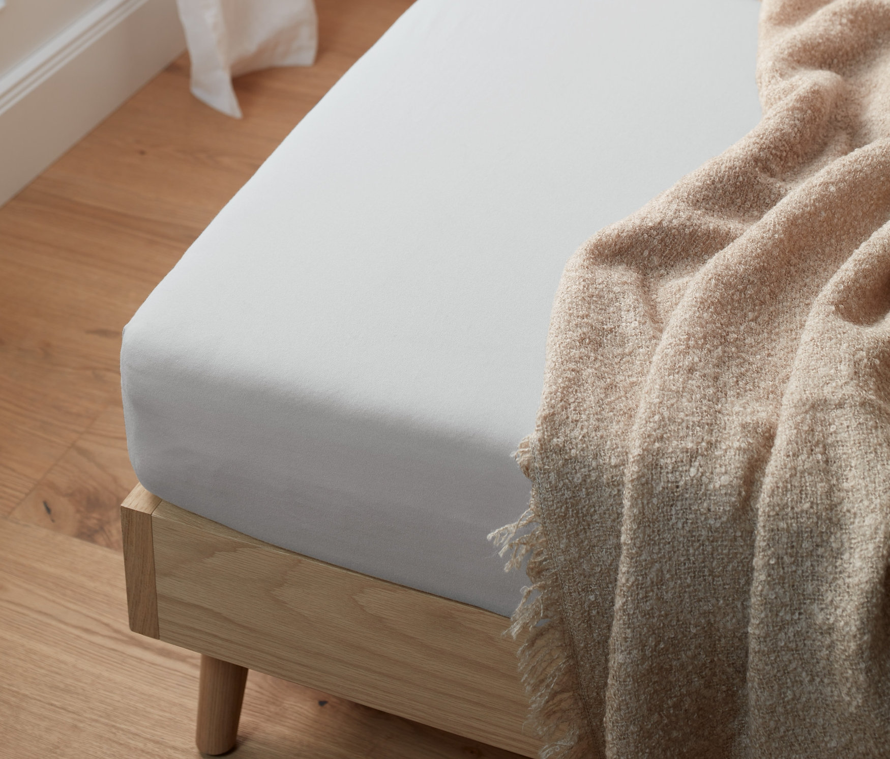 Açık gri, normal boy bir jersey lastikli çarşaf, üzerine bej bir battaniye örtülmüş bir yatak üzerinde duruyor.