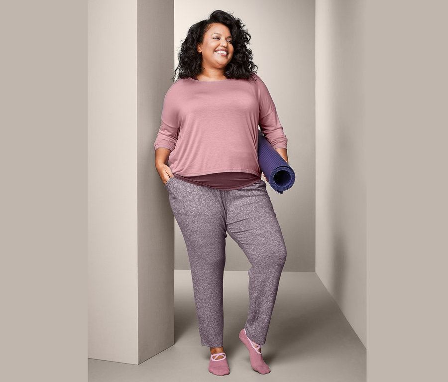 Kadın rulo halinde bir egzersiz matı tutuyor, 2'si 1 Arada Spor Tişörtü ve Rahat Pantolon giyiyor.