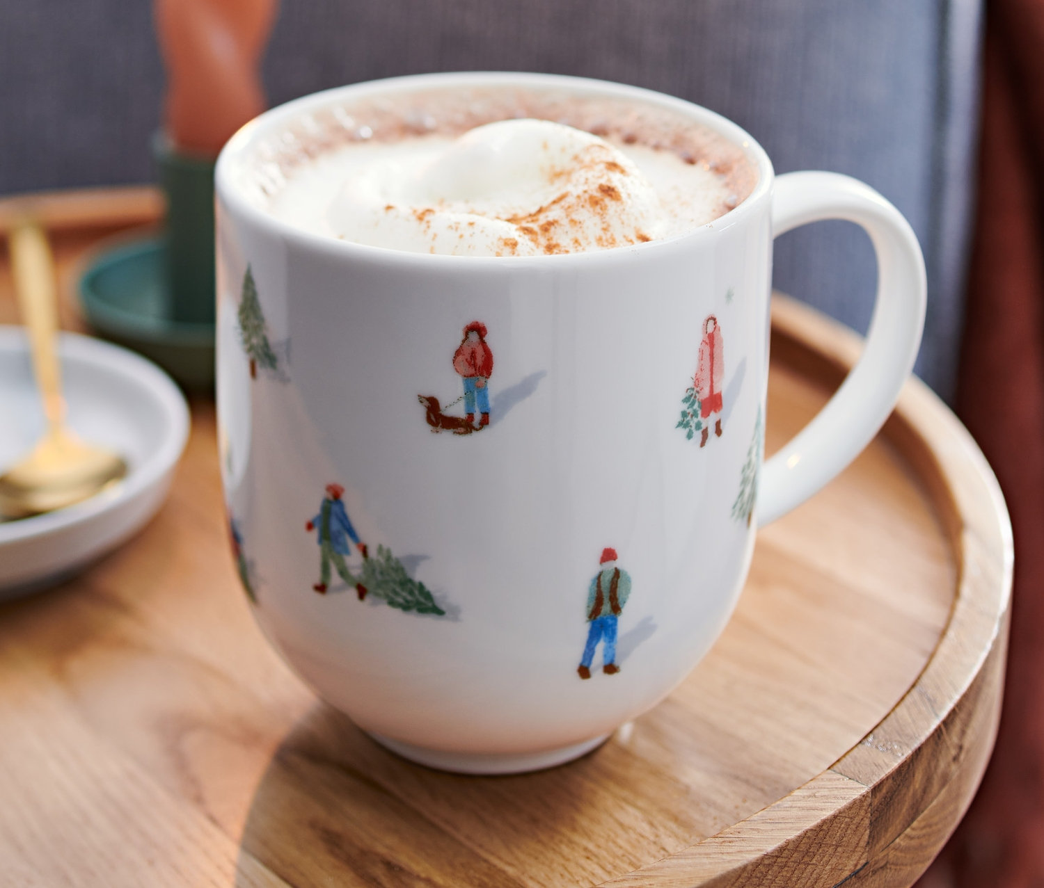 Ahşap bir masanın üzerinde sıcak içecek ve krem şanti bulunan Jumbo Fincan duruyor. Arka planda yanan bir mum ve bir kanepenin bir kısmı var.