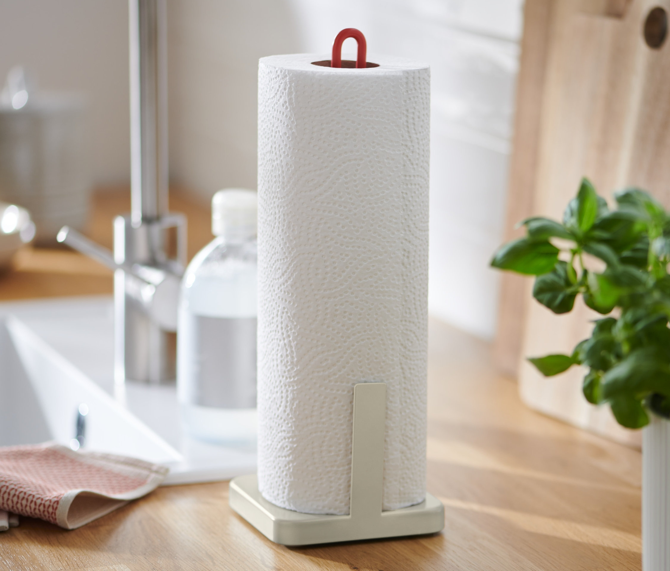 Mutfak tezgahında kağıt havlu tutucu, lavabo, sabunluk ve saksıda fesleğen bulunmaktadır.