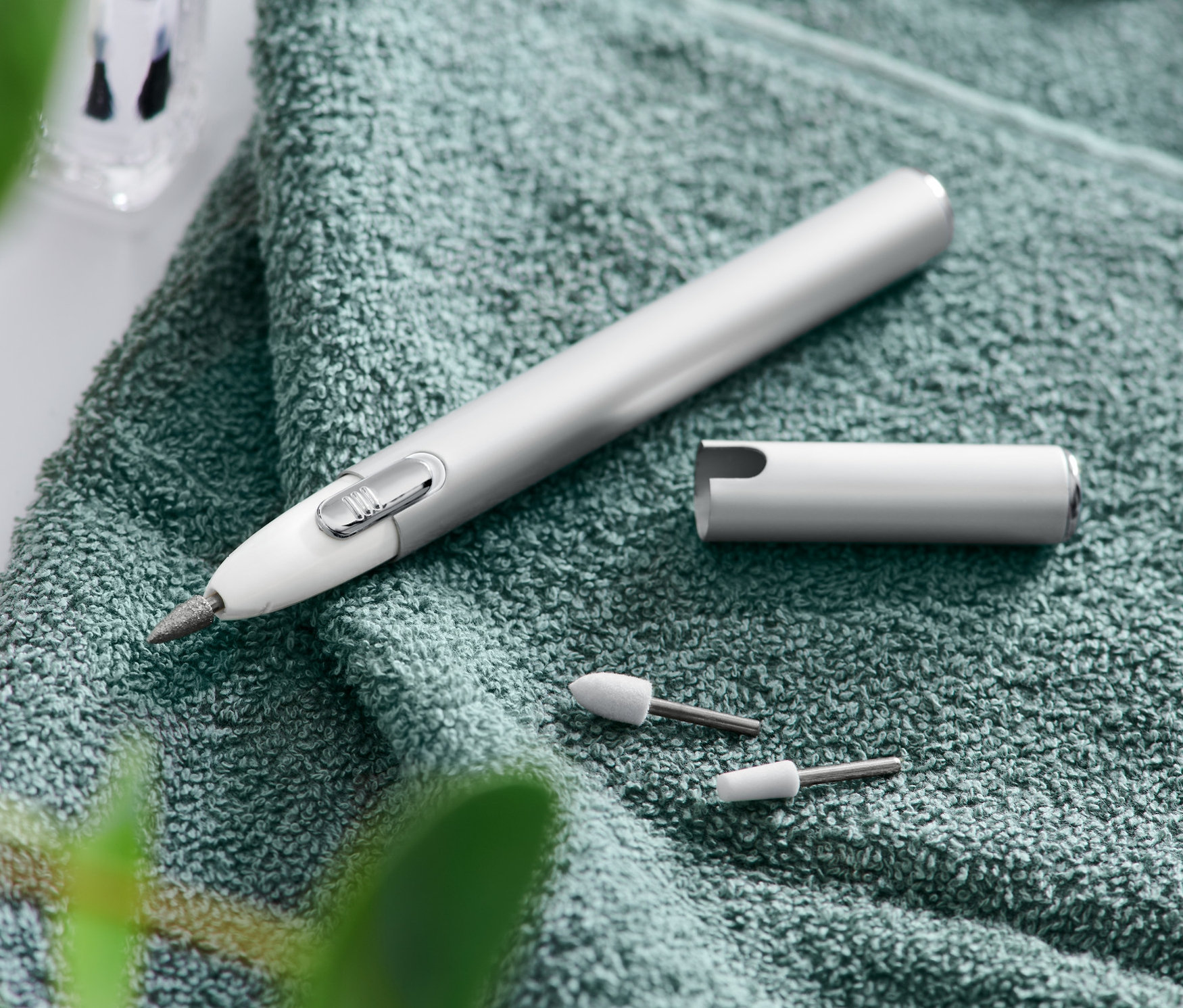 Manikür ve pedikür aleti, başlıkların, törpünün ve makasın yanında yeşil bir havlu üzerinde duruyor.