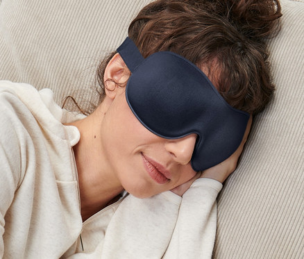 Kadın koltukta uyuyor, gözünde uyku maskesi var.