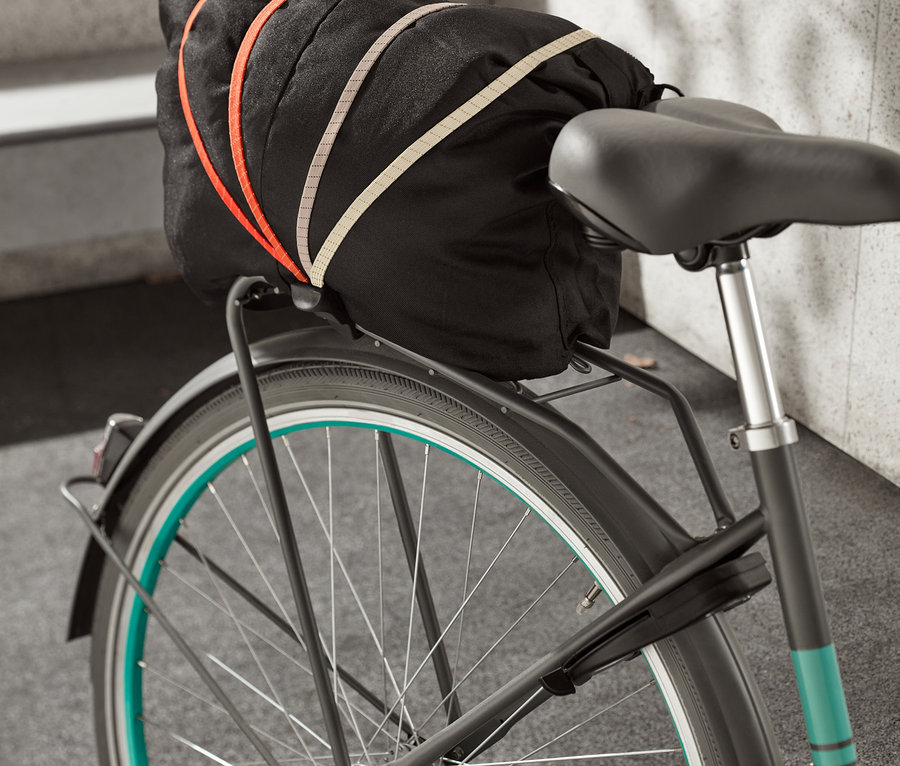 Bisiklet sabitleme kayışı, bir bisikletin bagajındaki siyah bir çantayı sabitliyor.