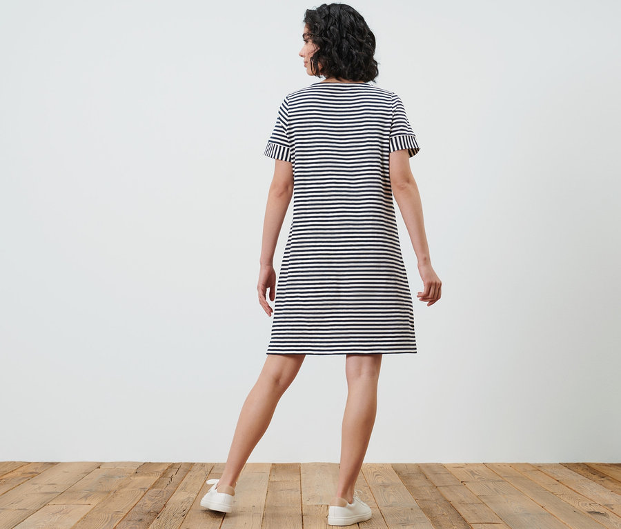 Kadın kameraya arkası dönük duruyor ve çizgili jarse bir elbise giyiyor.