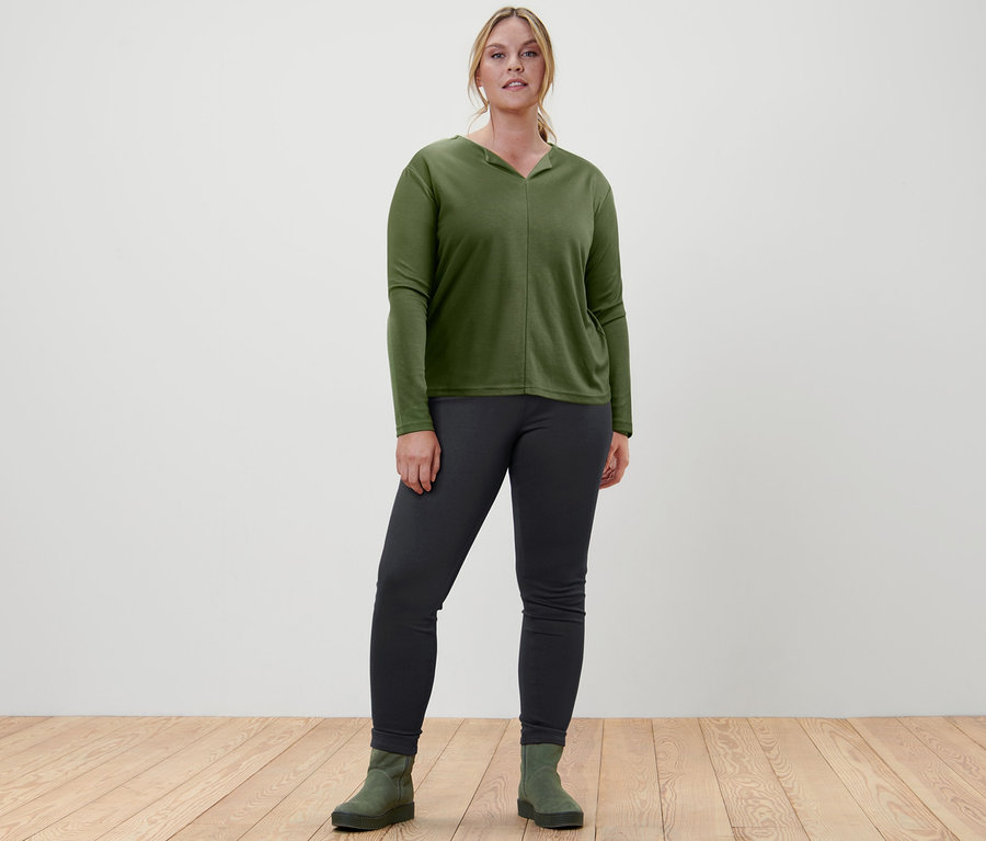 Bir kadın jegging, bluz ve süet bot giyiyor.