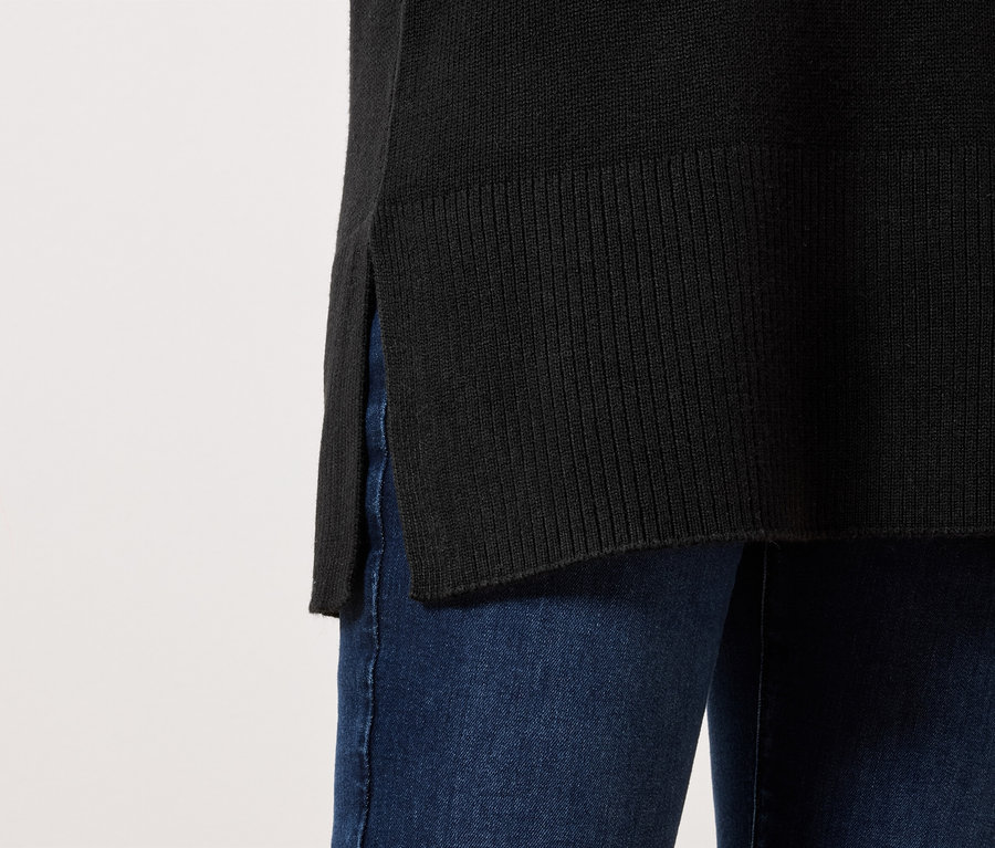 Yan yırtmaçlı siyah kazak, mavi kot pantolonla giyilmiş.