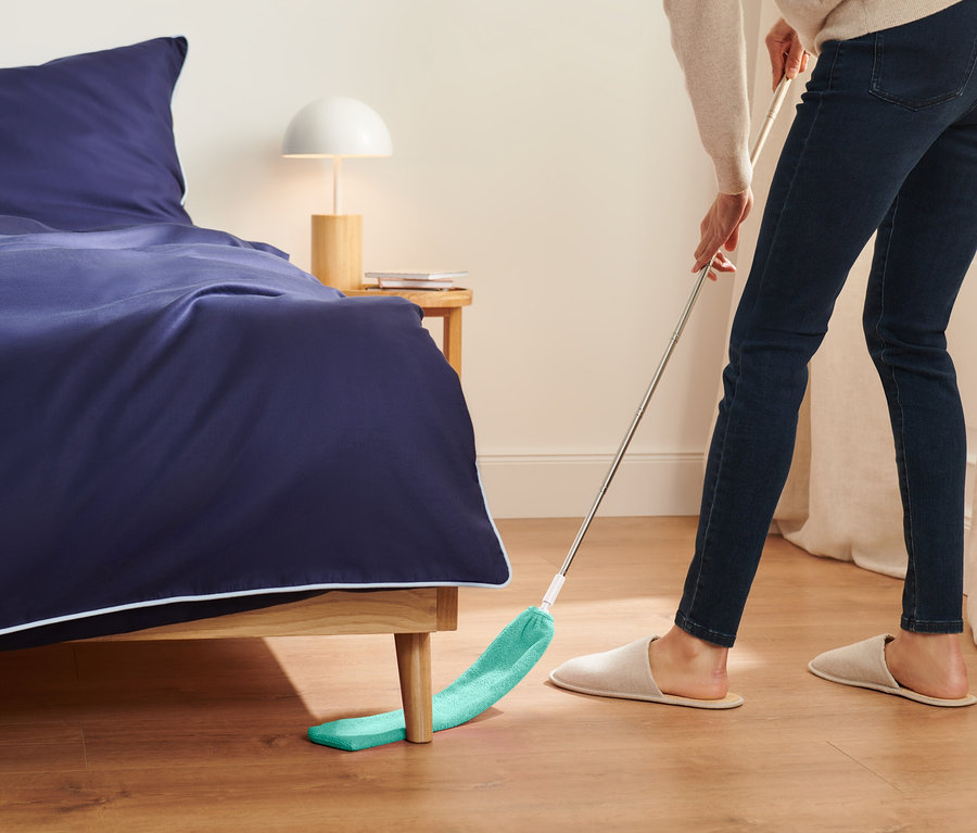 Kadın, yatağın altını yeşil bir paspasla temizliyor.