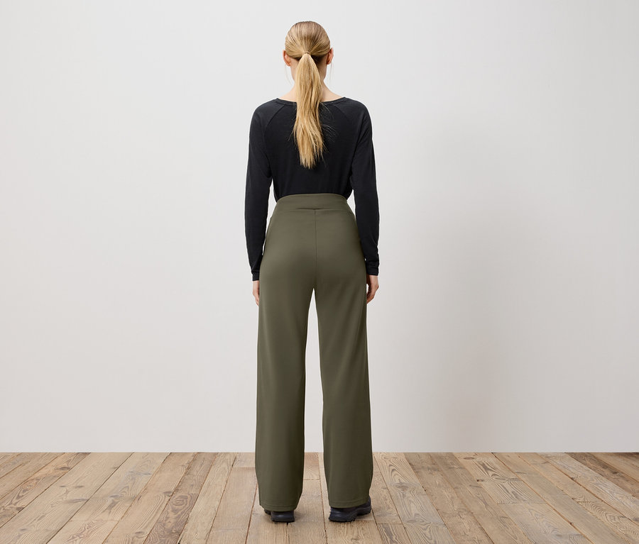 Atkuyruklu bir kadın, arkadan görünümü, siyah uzun kollu bir bluz ve zeytin yeşili pantolon giyiyor.