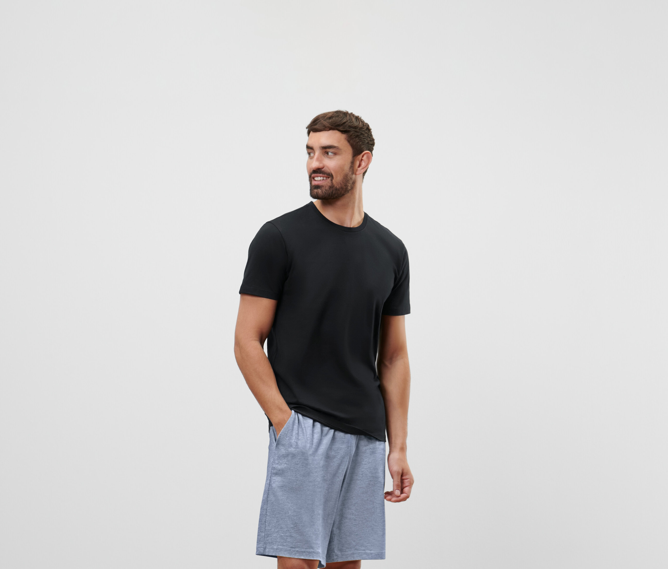 Siyah tişörtlü ve gri şortlu bir adam sağa bakıyor.