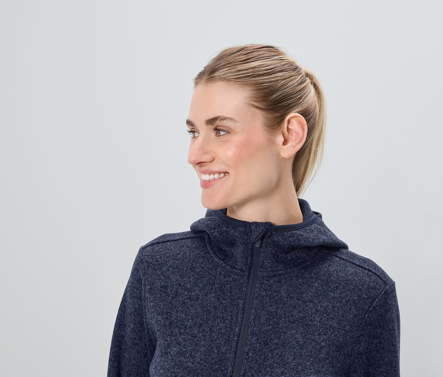 Mavi fermuarlı kapüşonlu sweatshirt giyen sarışın saçlı gülümseyen bir kadının profil görüntüsü.