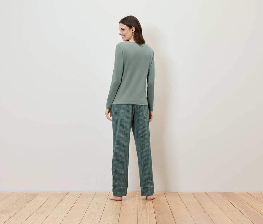 Desenli pantolon ve uzun kollu yeşil pijamasıyla bir kadın kameraya arkası dönük duruyor.