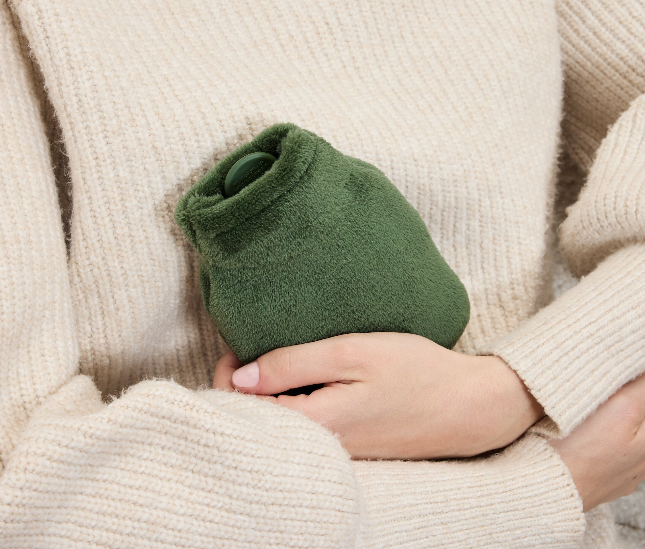 Kazaklı bir kadın ellerinde yeşil, tüylü bir sıcak su torbası tutuyor.