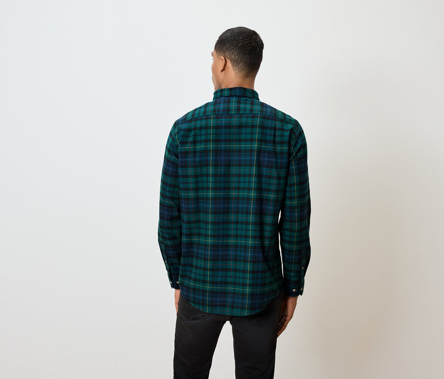 Sırtı kameraya dönük bir adam, yeşil ekose gömlek ve siyah kot pantolon giyiyor.