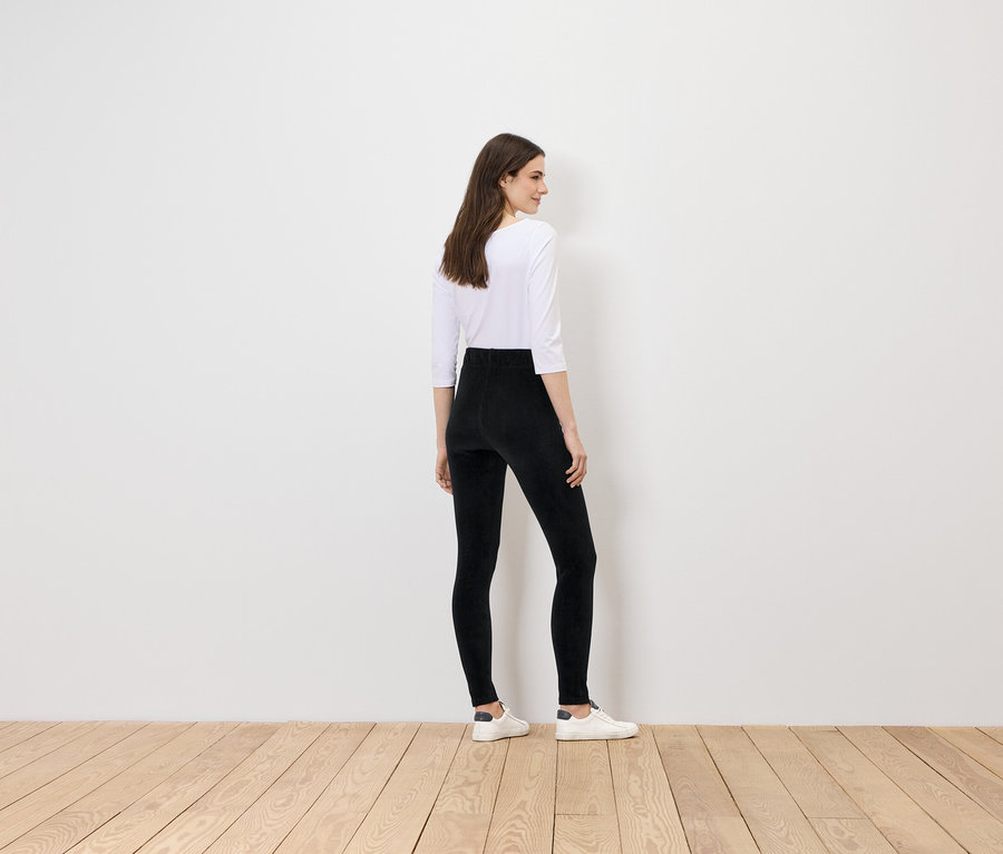 Siyah tayt ve beyaz üst giyen bir kadın kameraya arkası dönük duruyor.