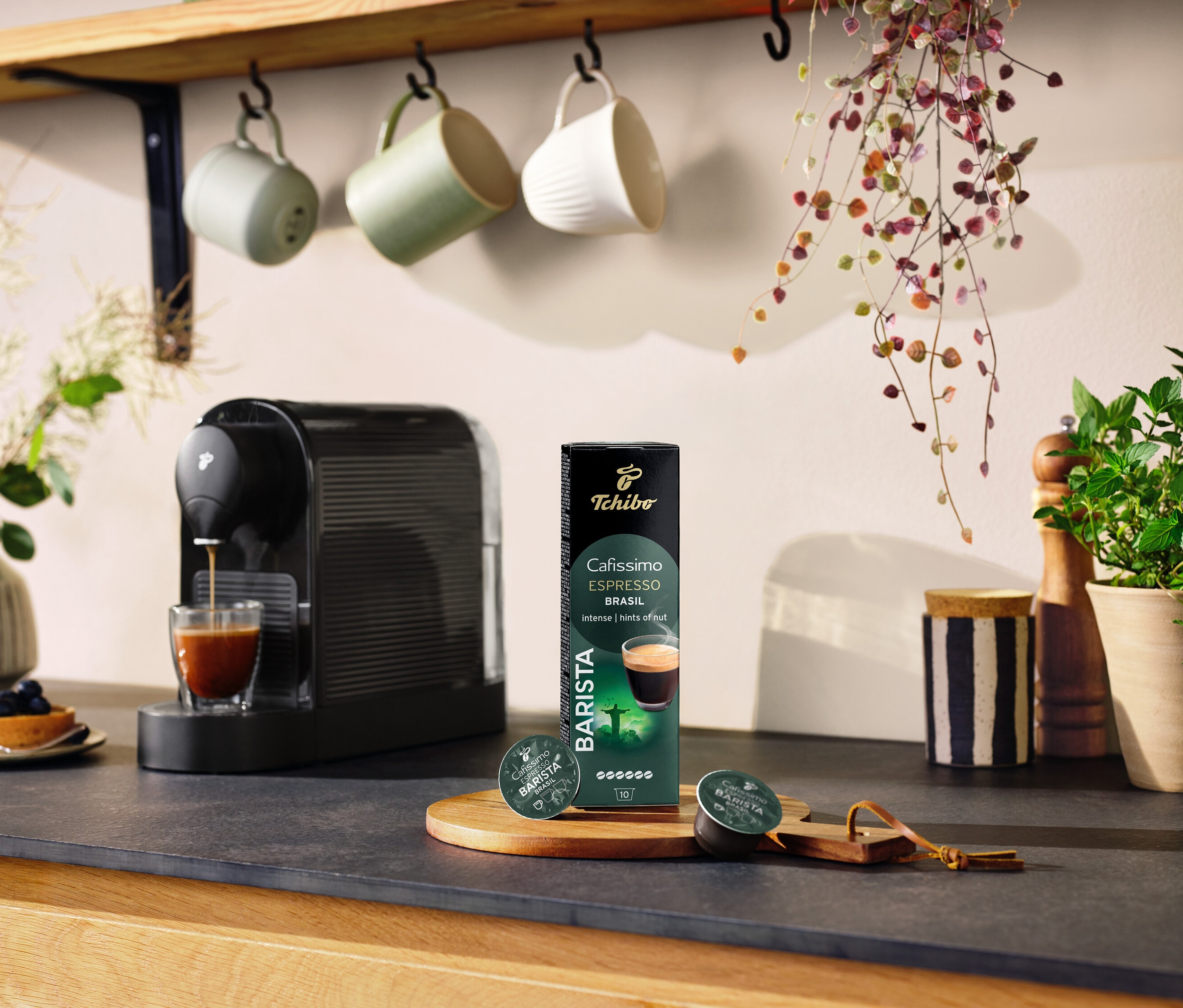 Siyah kahve makinesi, bir bardakta kahve hazırlıyor ve yanında Espresso Brasil – 10 Kapsül paketi bulunuyor.