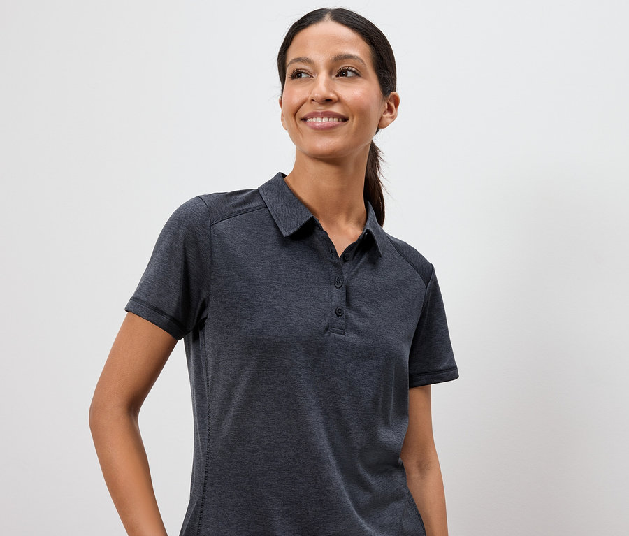 Kadın beyaz bir arka plan önünde koyu gri bir polo tişört giyiyor.