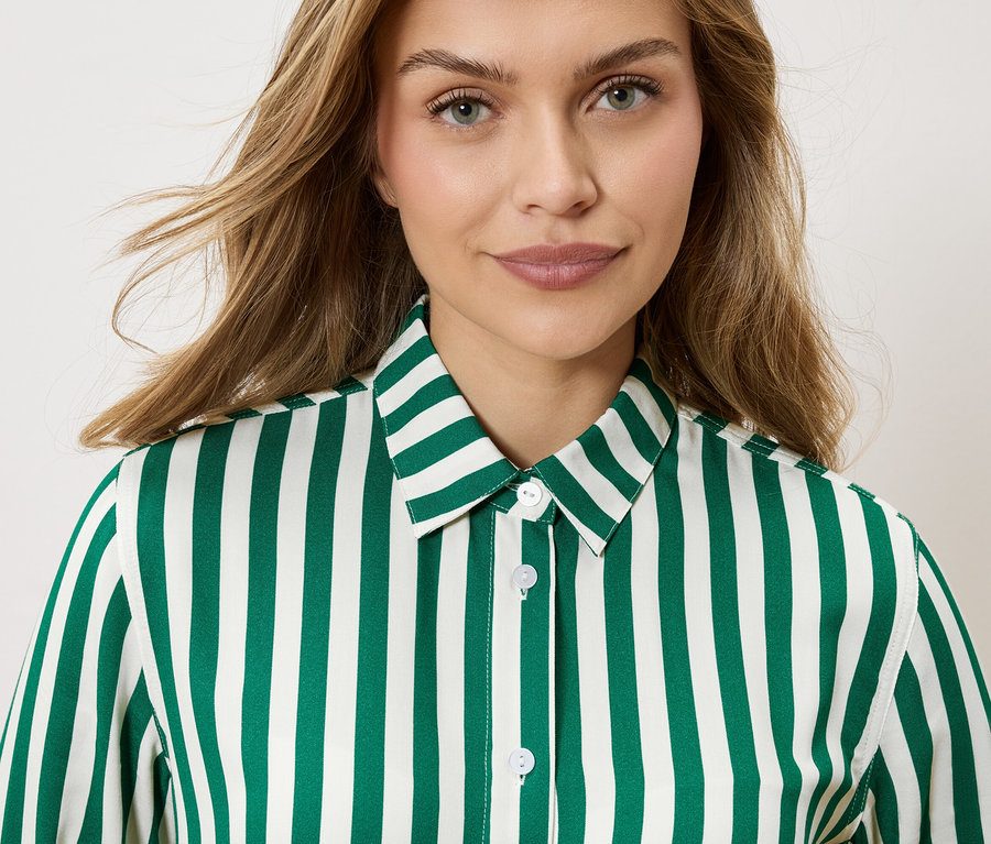 Smar yeşili ve beyaz çizgili bir gömlek giyen sarı, dalgalı saçlı bir kadının portresi.