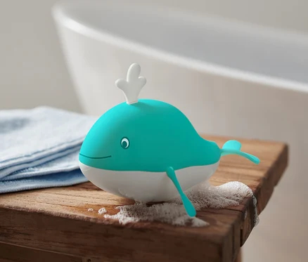 Kurmalı Balina Banyo Oyuncağı, ahşap bir tabure üzerinde, yanında mavi bir bez ve köpük, arka planda bir küvet.