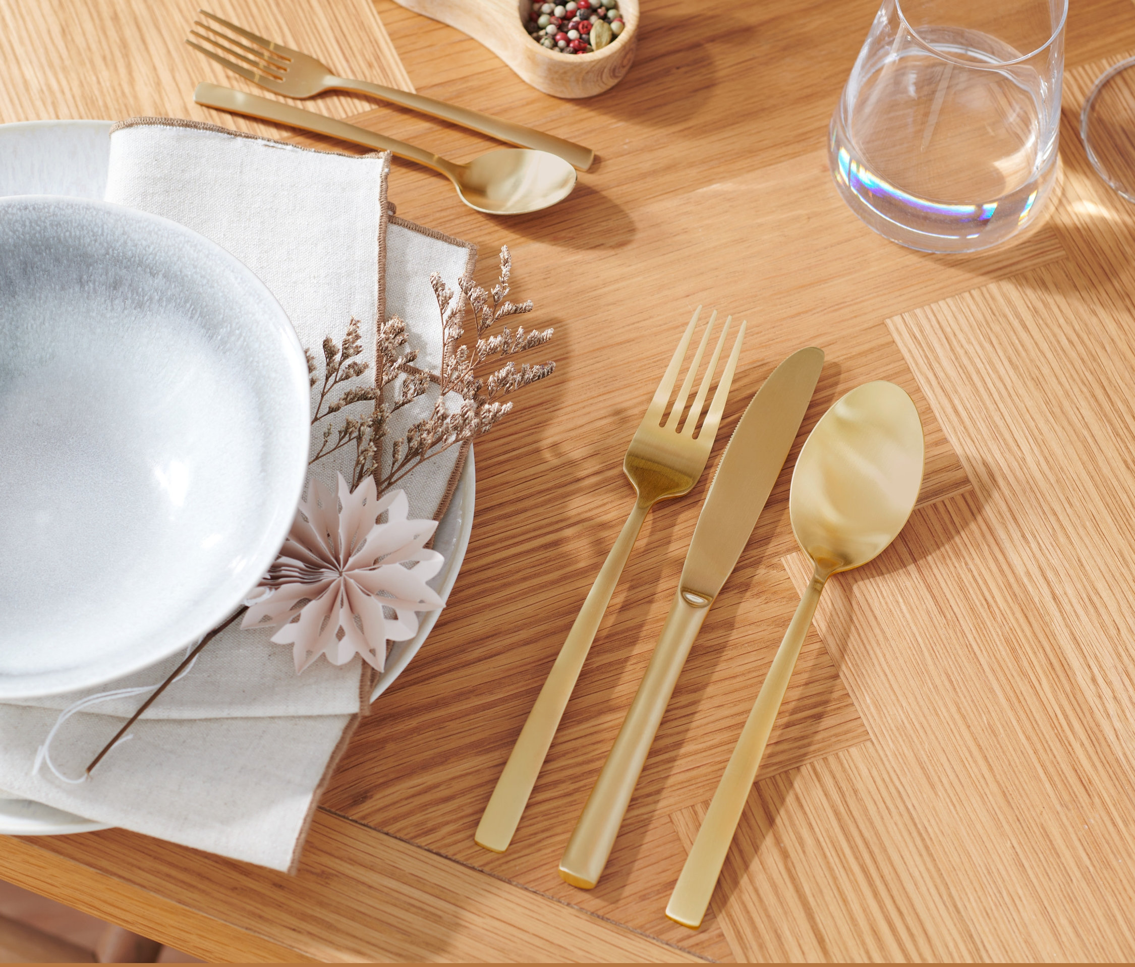 Ahşap bir masa üzerinde tabak, peçete ve 20 parça şampanya altın rengi çatal bıçak kaşık seti.