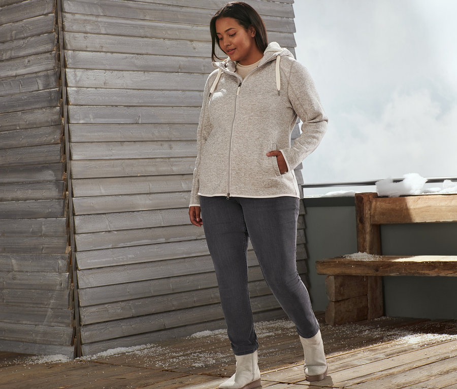 Bir kadın dışarıda duruyor ve bej Peluş Örgü Polar Hırka, Slimfit-Jeans ve süet botlar giyiyor.