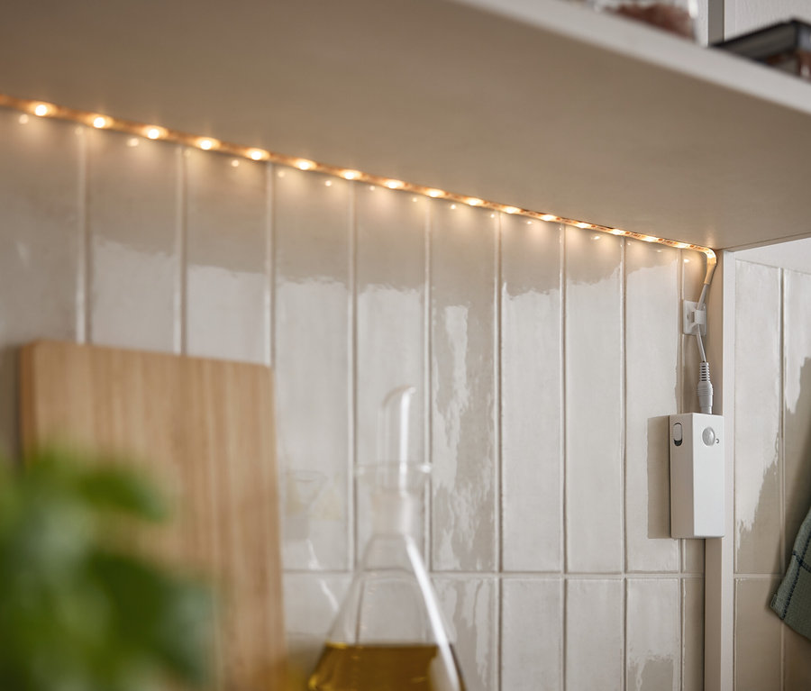 LED şerit, beyaz fayanslar üzerinde bir dolabın altında parlıyor.