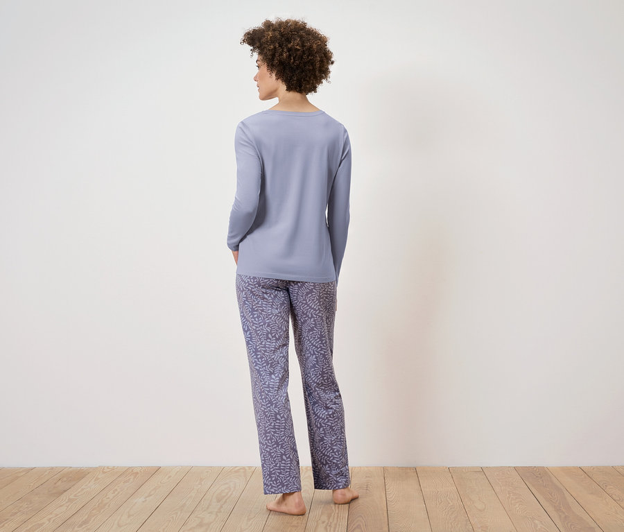 Kadın kameraya arkası dönük, açık mor uzun kollu pijama ve yaprak desenli pantolon giyiyor.