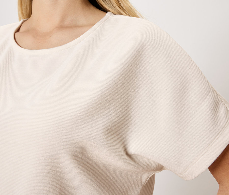 Yakın çekimde, yuvarlak yakalı, kısa kollu, açık bej bir bluz giyen bir kadın.