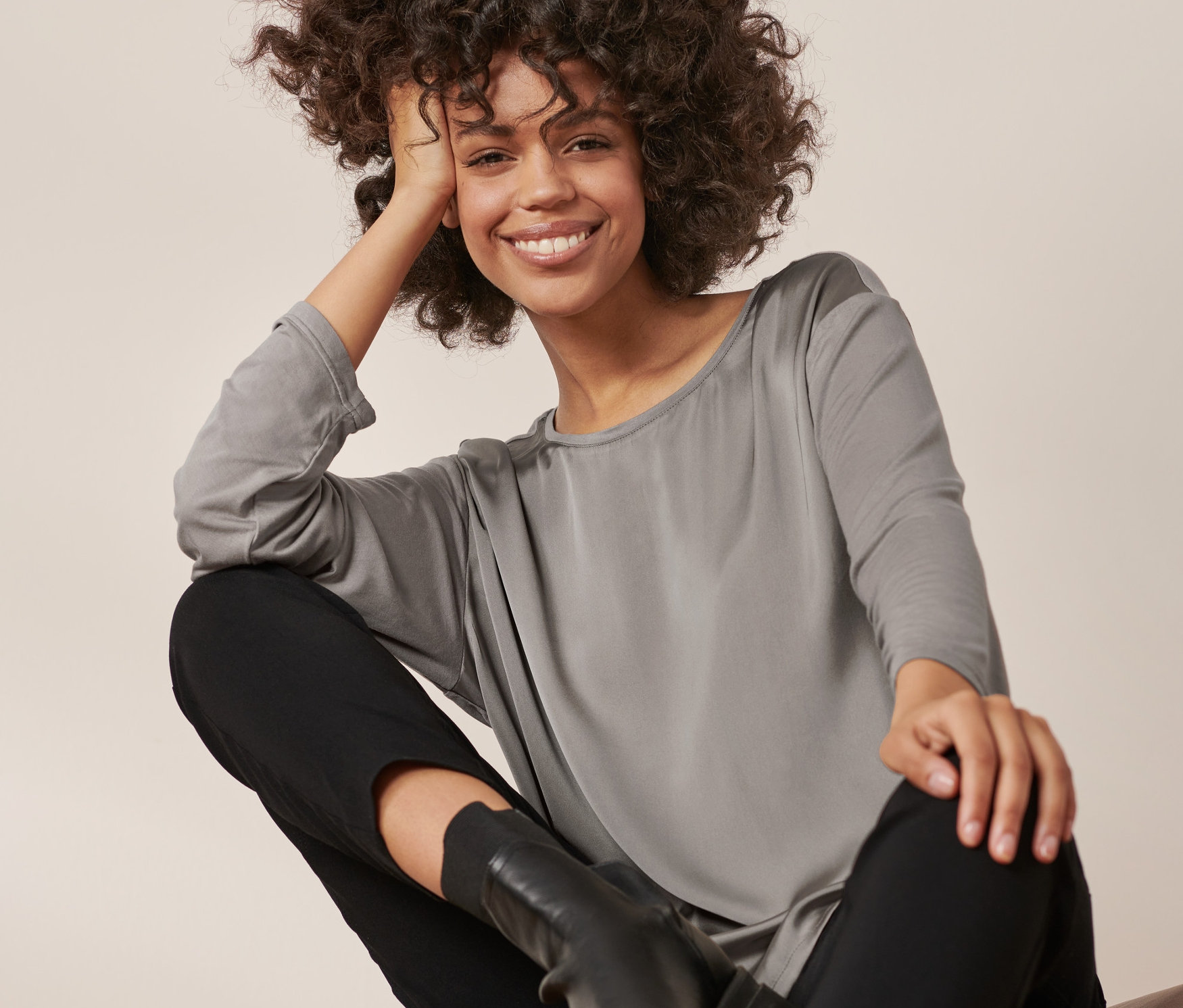 Kadın Karışımlı Bluz, siyah pantolon ve botlarla oturuyor ve poz veriyor.