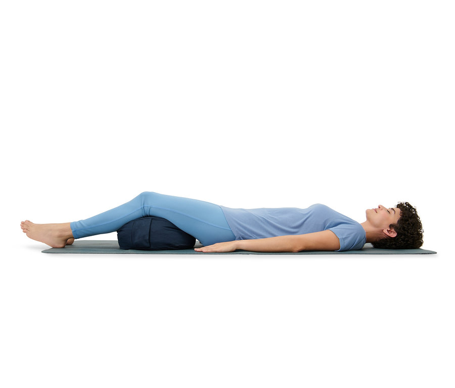 Kadın yerde matın üzerinde yatıyor, bacakları meditasyon minderi üzerinde.