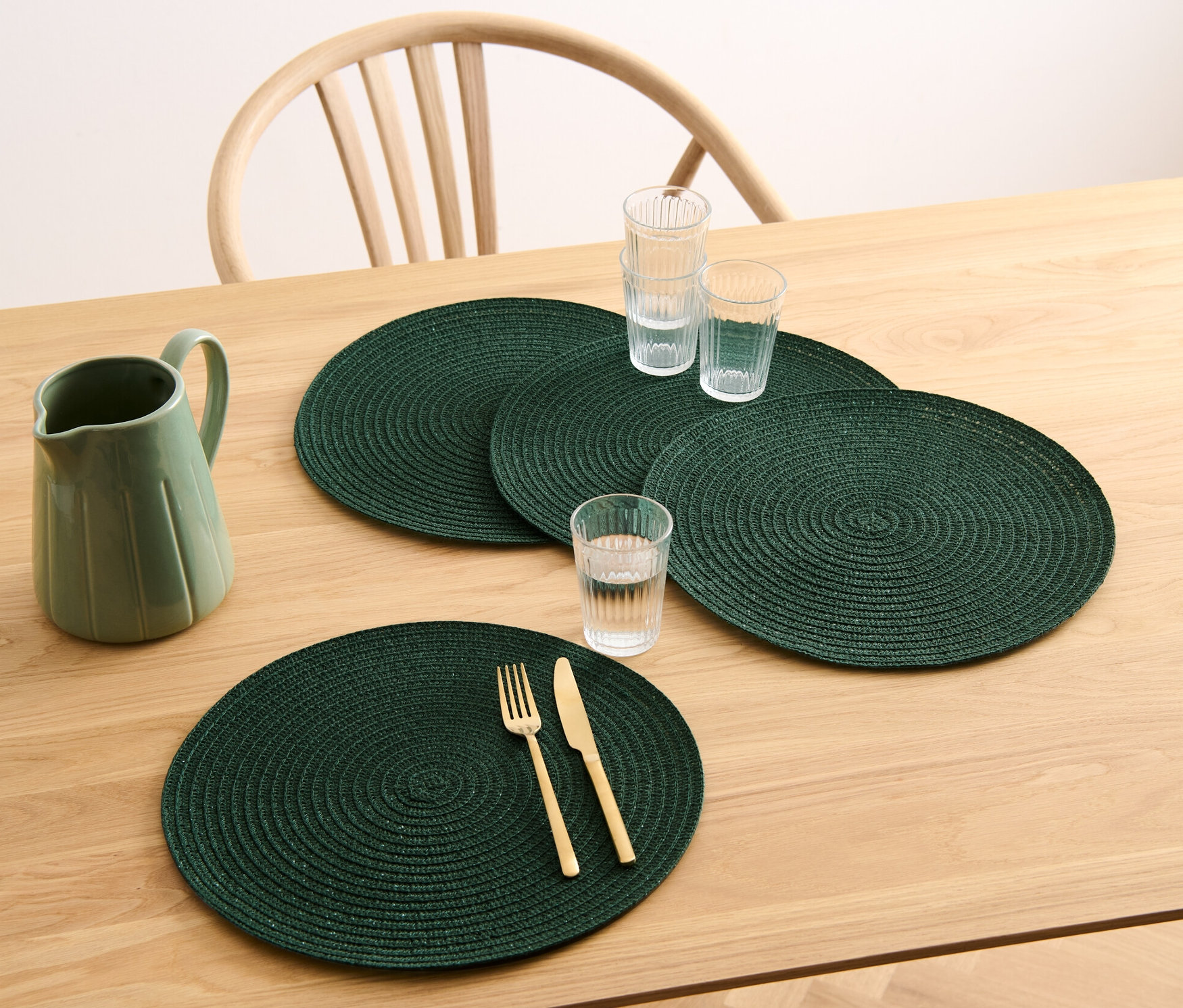 Ahşap bir masa üzerinde dört adet yeşil, yuvarlak Amerikan servis, bir sürahi ve bardaklar bulunmaktadır.