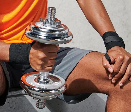 Adam fitness el bileği manşetleriyle oturuyor ve dambıl tutuyor.