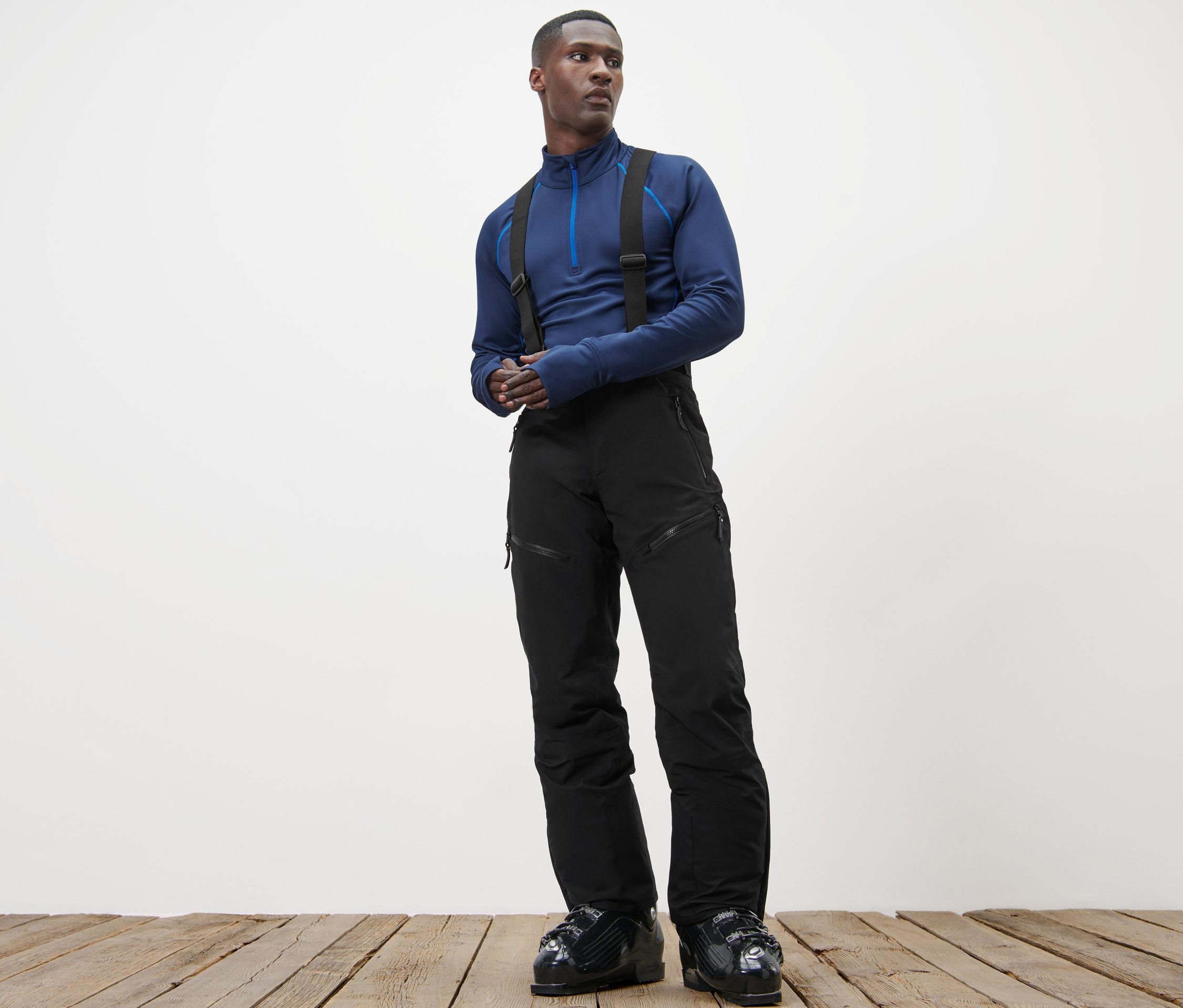 Tahta zeminde duran adam mavi bir üst ve Yüksek Teknolojili Kayak Pantolonu giyiyor.