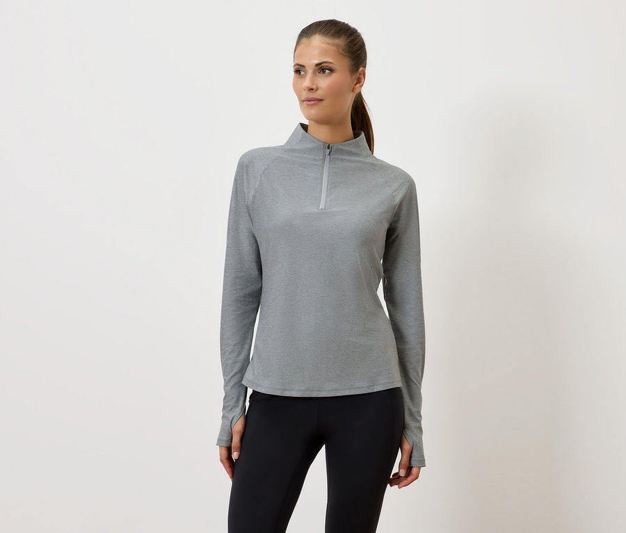 Gri fermuarlı sweatshirt ve siyah taytlı bir kadın beyaz bir arka planın önünde duruyor.