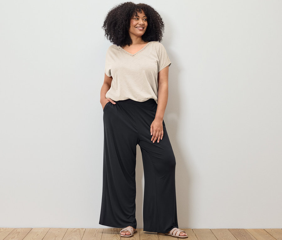 Kadın krem beyazı modal karışımlı bir tişört ve siyah palazzo pantolonla poz veriyor.