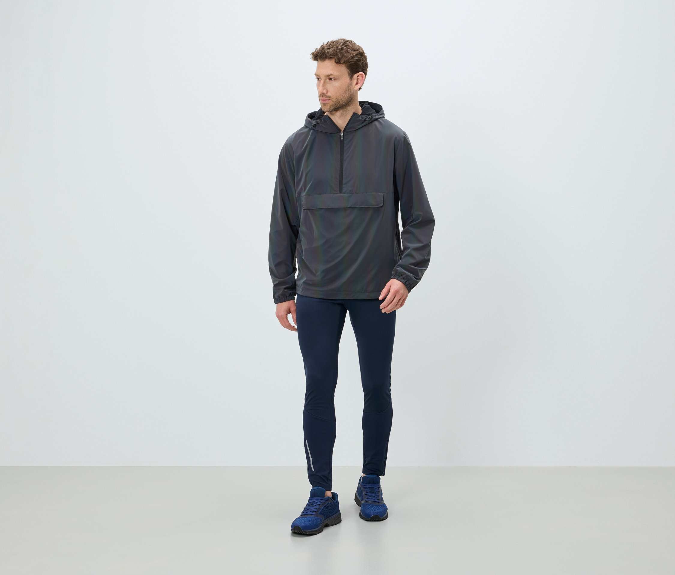 Adam gri kapüşonlu bir anorak, lacivert tayt ve mavi ayakkabılar giyiyor.