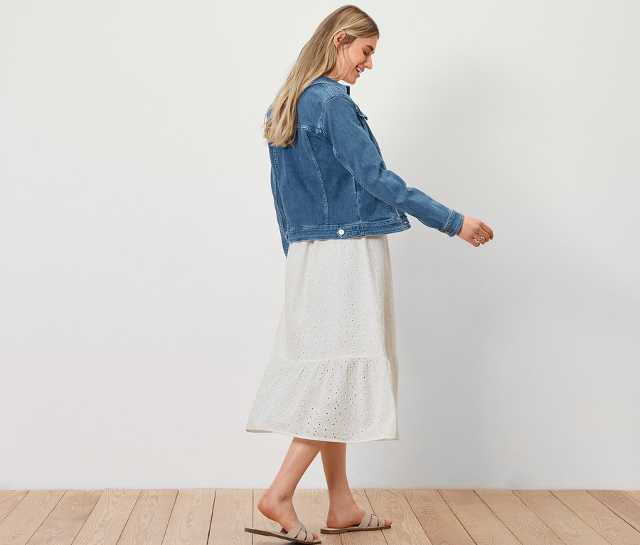 Kadın yürüyor, üzerinde Kot Ceket, Brodeli Bluz Elbise ve Hasır Görünümlü Alışveriş Çantası var.