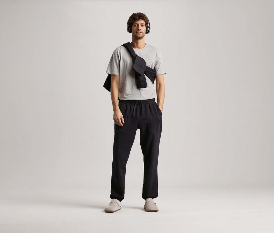 Kulaklıklı, gri tişörtlü ve siyah eşofman altı olan adam.