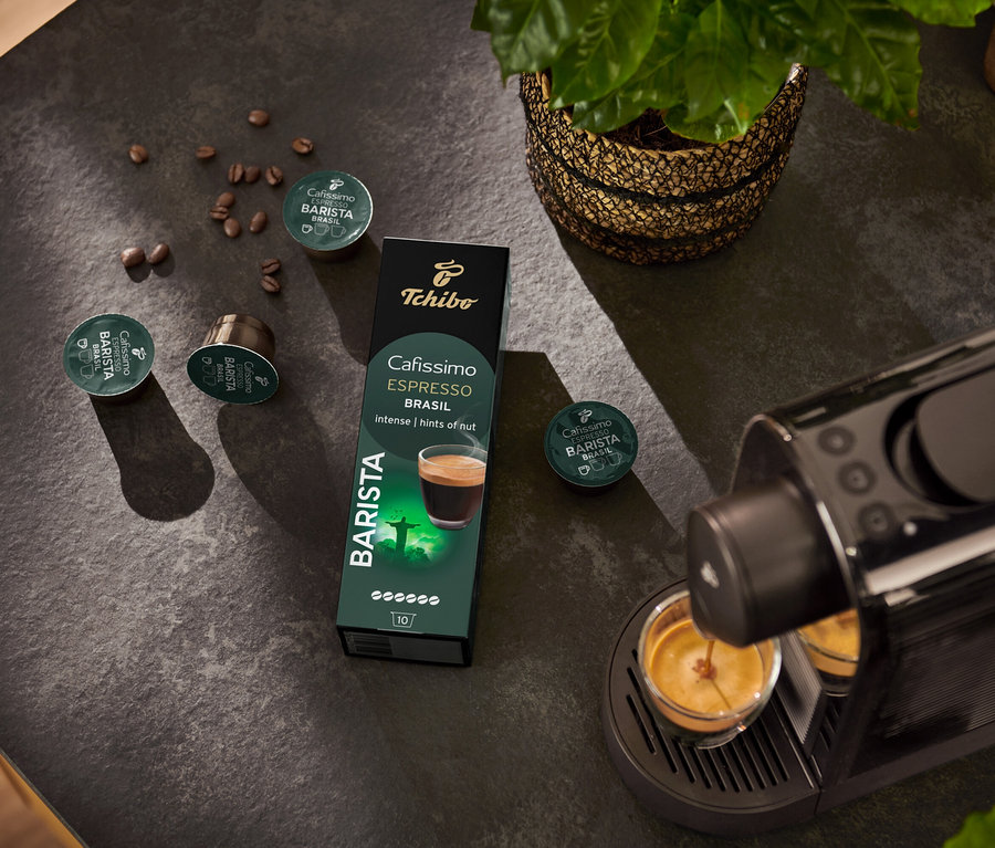 Espresso makinesi fincanı dolduruyor. Arka planda Espresso Brasil – 10 Kapsül paketi ve kahve çekirdeği.