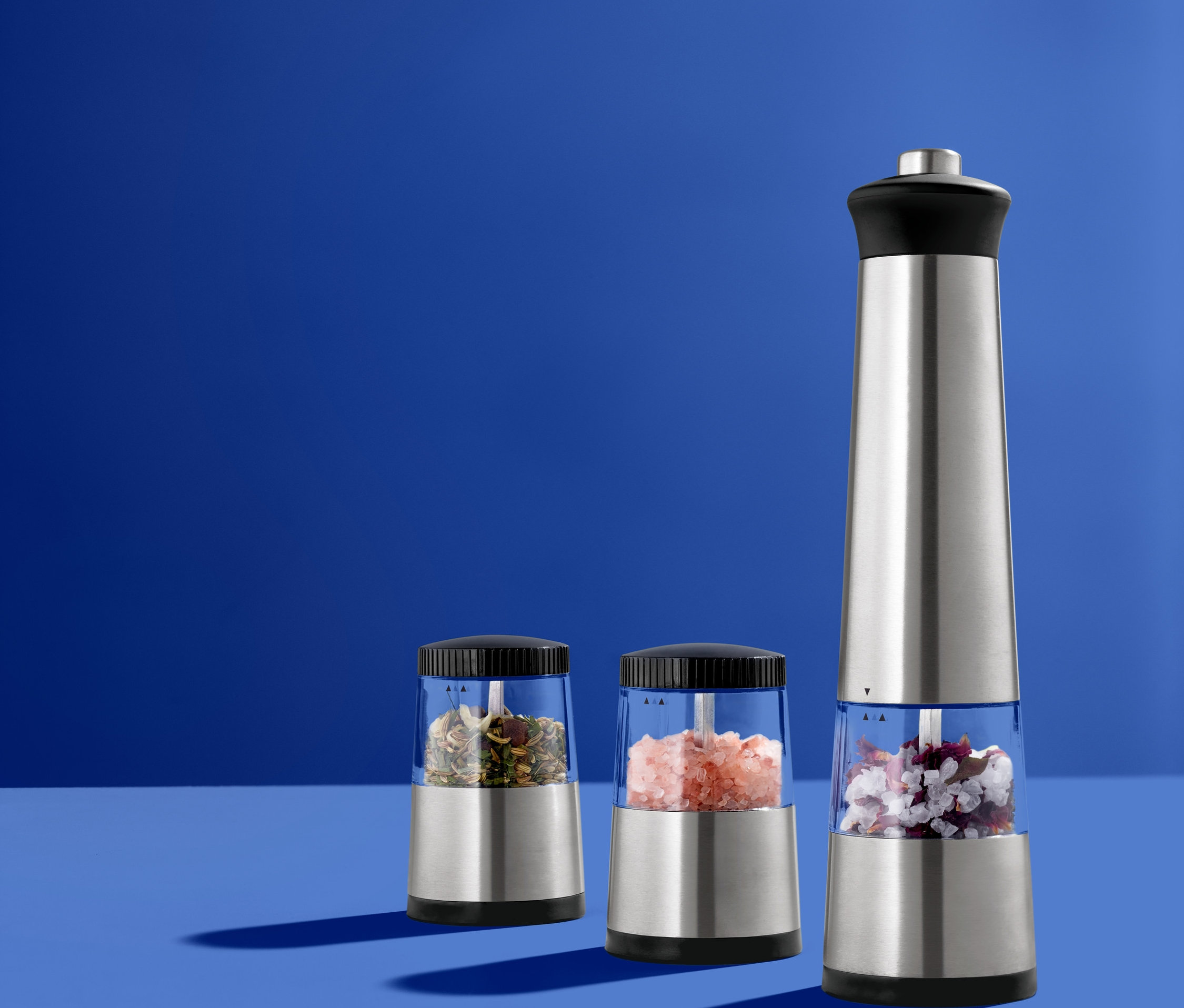 Mavi bir yüzeyde duran üç adet elektrikli baharat değirmeni. Bir büyük, iki küçük.