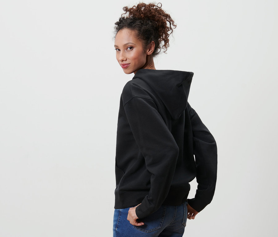 Kadın omzunun üzerinden bakıyor, üzerinde siyah bir kapüşonlu ve kot pantolon var.