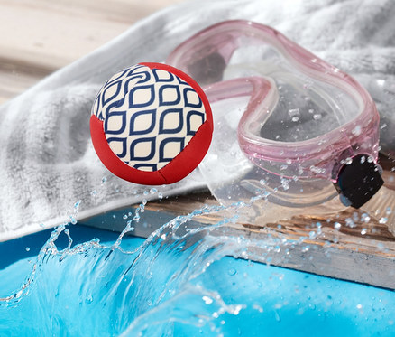 Zıplayan su topu, havuz kenarında bir havlu ve yüzme gözlüğünün yanında duruyor.